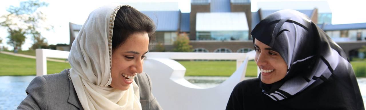 Photo of two female students sitting outside, smiling together.